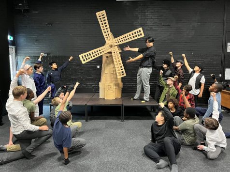 A group of people sitting on a stage with a person standing in front of a windmill

AI-generated content may be incorrect.